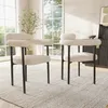 Two beige upholstered chairs with black metal legs are placed on a textured rug in a well-lit room with large windows. Podgląd zdjęcia produktu