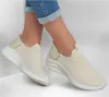 A pair of beige Skechers slip-on sneakers worn by a person, shown from the ankle down, with blue jeans rolled up at the cuffs. Náhled obrázku produktu