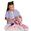 A young girl is styling the hair of a toy dog on a pink table. Podgląd zdjęcia produktu