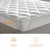 Close-up of a white mattress topper on a bed, with an orange measurement indicator and two feature icons at the bottom. Produktbild-Vorschau