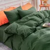 A close-up view of a bed with dark green and orange bedding. Produktbild-Vorschau