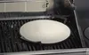 A close-up shot of a round pizza stone with handles, placed on a grill grate inside a grill. Podgląd zdjęcia produktu