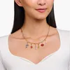 A woman wearing a white top and a gold chain necklace with various charms. Anteprima dell’immagine prodotto