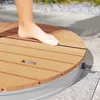 A person's foot is shown standing on a circular wooden outdoor shower base. Produktbild-Vorschau