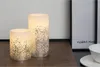 Two LED candles with glitter on a wooden surface. Produktbild-Vorschau