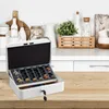 A white cash box with a coin tray is open on a wooden table, with kitchen cabinets and shelves in the background. Produktbild-Vorschau