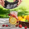 A person is holding an ice cube tray over a pitcher of fruit-infused water, with various fruits in the background. Náhled obrázku produktu