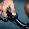 A close-up shot of a person's hand pressing a red button on a bicycle handlebar. Náhled obrázku produktu