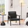 A black armchair with wooden armrests is placed in a room with a window, a floor lamp, and a side table with a drink. Produktbild-Vorschau