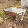 Silberner tragbarer Campinggrill mit Maschendrahtrost, auf trockenen Blättern und Gras neben einem Baumstamm aufgestellt Anteprima dell’immagine prodotto