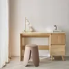 A minimalist desk setup with a wooden desk, a pink stool, a gold lamp, and some stationery. Produktbild-Vorschau