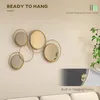 A decorative metal wall mirror with multiple circular frames and mirrored inserts, displayed on a wall above a sofa. Produktbild-Vorschau