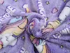 A close-up view of a soft, purple blanket with a unicorn and star pattern. The blanket is folded and creased, showing its plush texture. Náhled obrázku produktu