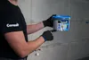 A person in gloves points to a bucket of Ceresit Fugenmörtel. Produktbild-Vorschau