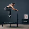 A woman is jumping on a mini-trampoline with a handle in a room. Voir les images du produit