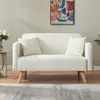 A beige sofa with two white cushions is shown in a room with a painting on the wall and a rug on the floor. Anteprima dell’immagine prodotto