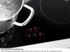 A close-up shot of a black induction hob with a pot of boiling water on it. The control panel with red digital displays is visible. Produktbild-Vorschau