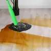 A green mop with a black mop head is cleaning up a spill of brown liquid on a light-colored wooden floor. Voir les images du produit