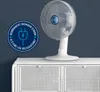 A white table fan is displayed on a white cabinet against a dark blue wall. A circular graphic with text and an electrical plug icon is overlaid on the left side of the image. Náhľad obrázku produktu