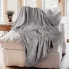 A gray plush blanket is draped over a white sofa with a textured gray pillow. Produktbild-Vorschau