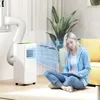 A woman is sitting on the floor in front of a portable air conditioner, working on a tablet. The air conditioner is blowing cool air. Náhled obrázku produktu