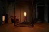 A vintage-style Edison bulb lamp with a copper base and black metal frame sits on a wooden table in a dimly lit room with antique furniture. Anteprima dell’immagine prodotto