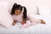 A young girl is lying on a bed with a pink stuffed unicorn. Produktbild-Vorschau