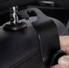 A hand is holding a black car seat organizer hook that attaches to the headrest. Produktbild-Vorschau