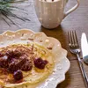 A breakfast setting with a pancake, cherries, chocolate shavings, and a mug of hot chocolate. Voir les images du produit