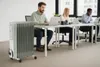 Three people working at desks in an office setting, with a portable heater in the foreground. Podgląd zdjęcia produktu