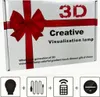 The image shows the packaging of a 3D visualization lamp, with a red ribbon and bow design. Below the main box image, there are four smaller images depicting the components of the lamp: a bulb, a USB cable, a remote control, and a dimmer switch. Voir les images du produit