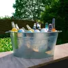 A galvanized metal tub filled with bottles and ice, set outdoors with greenery in the background. Voir les images du produit