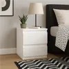 A white nightstand with two drawers next to a bed. Produktbild-Vorschau