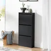 A black shoe cabinet with three flip-down drawers is shown against a white wall with a window and curtains in the background. A woven basket with blankets and pillows is placed next to the cabinet. Náhľad obrázku produktu