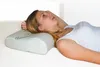 A woman lying on her back on a white surface, resting her head on a pillow. Produktbild-Vorschau