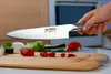 A hand holding a Global G-2 chef's knife over a cutting board with chopped red peppers and sushi. Anteprima dell’immagine prodotto