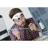 A man is using a magnifying headband with LED lights to solder a circuit board, which is part of a larger electronic device. Produktbild-Vorschau