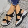 Schwarz-weiße Komfortsandalen mit geknoteten Stoffriemen an den Füßen einer Person, mit getragener blauer Jeans Anteprima dell’immagine prodotto