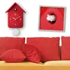 A red cuckoo clock and a red framed picture with a bird are displayed on a white wall above a yellow sofa with red cushions. Produktbild-Vorschau
