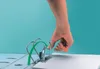 A hand is shown pressing down on the rings of a binder to open them, with green arrows indicating the motion. Produktbild-Vorschau