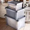 Three plastic storage boxes stacked on a wooden floor, with a white chair and a soccer ball in the background. Produktbild-Vorschau