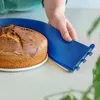 A hand is holding a blue cake carrier over a cake on a white plate. Produktbild-Vorschau