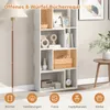 A white bookshelf with multiple compartments, some of which are a light orange color, is shown in a room. The bookshelf is decorated with various items including books, decorative objects, framed pictures, a plant, a basket, a radio, and a clock. A floor l Podgląd zdjęcia produktu