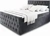 A gray upholstered box spring bed with white bedding and pillows, shown from a diagonal angle against a white background. Produktbild-Vorschau