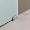 A close-up view of the bottom corner of a glass sliding door, showing a silver metal fitting attached to the floor. Produktbild-Vorschau