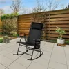A black rocking chair is placed on a tiled patio in a backyard setting, with a wooden fence and greenery in the background. Produktbild-Vorschau