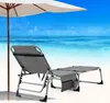 A grey beach chair with an extended leg rest sits on a sandy beach under a white umbrella, with the ocean and blue sky in the background. Náhled obrázku produktu