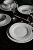 A formal table setting with white porcelain plates, bowls, and wine glasses on a black tablecloth, decorated with red peppercorns. Náhľad obrázku produktu