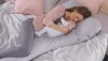 A woman is lying on a bed, breastfeeding a baby. She is using a long pillow for support. Produktbild-Vorschau