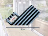A blue and black striped mop head is laid out on a wooden surface next to a window. Produktbild-Vorschau